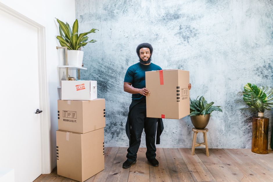 A person sits thoughtfully on the floor of a nearly empty room with a few moving boxes, gazing out a window, representing the emotional stress of selling a home.