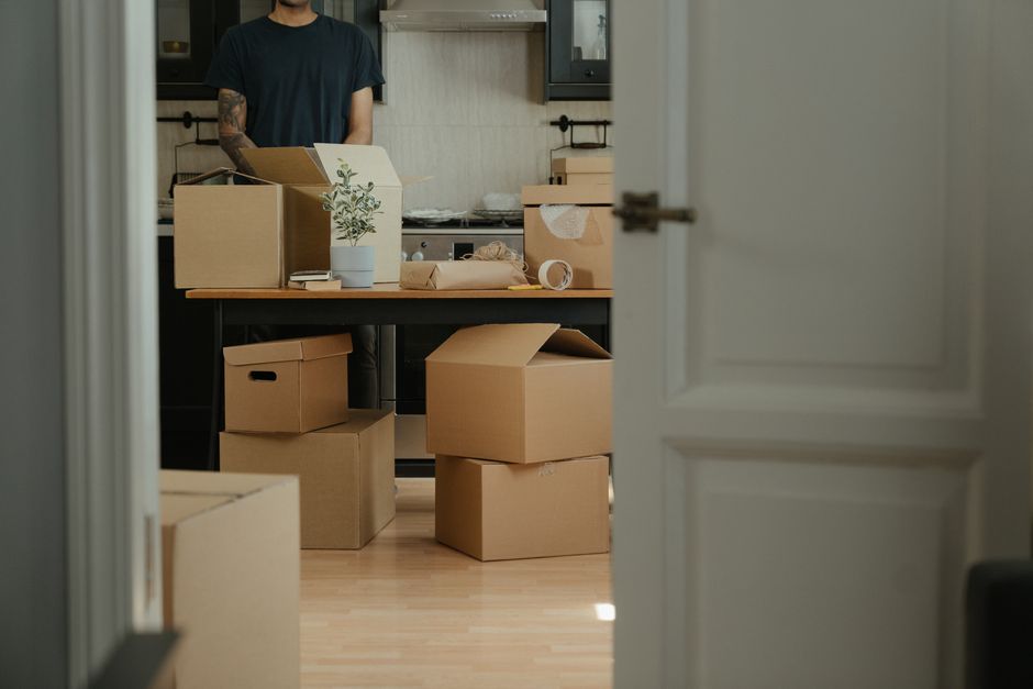 A person takes a healthy break while packing, eating a vibrant salad on the floor amidst moving boxes, illustrating the importance of nutrition during stressful times.